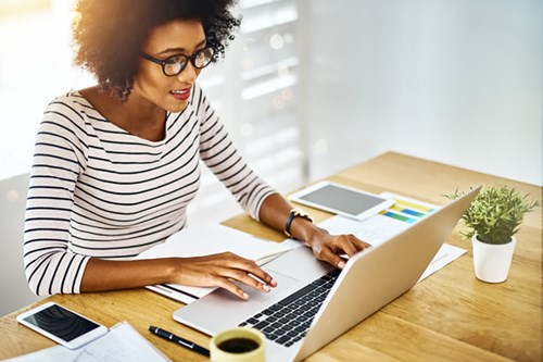 a woman in a striped shirt sitting at a desk and working on a laptop computer